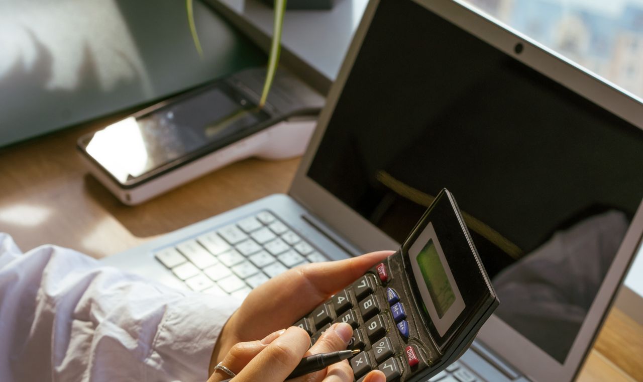 Mão segurando uma calculadora ao lado de um notebook